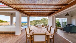 A covered outdoor dining area with a wooden table and chairs, a sofa, and a view of the sea. - Villa AU PAILLE EN QUEUE – Tranquil Escape with Ocean Views in St. Jean (Gustavia)