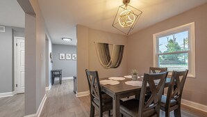 A dining area with a wooden table, four chairs, and a modern pendant light. - Koselig Retreat (Randallstown)