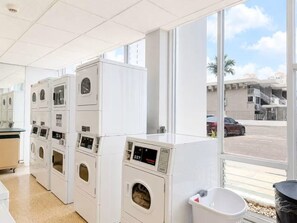 A laundry facility with multiple washing machines and dryers, a trash bin, and a view of a parking area through large windows. - Balcony for 2 Oceanview Balcony Pool Beach Parking Condado (San Juan)