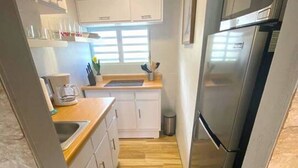 Una cocina estrecha con armarios blancos, una encimera de madera, un tapete negro y un refrigerador de acero inoxidable.
