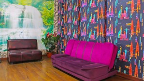 A living room with a purple sofa, a brown leather couch, and a waterfall mural on the wall.