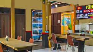 A hotel lobby with a reception desk, a large dining table with chairs, and a wall with various hotel advertisements.