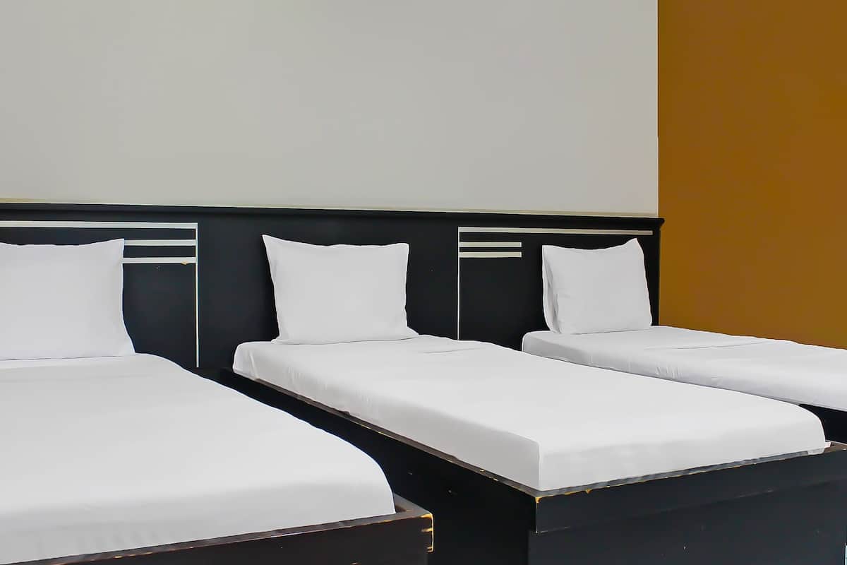 A hotel room with three single beds, each with white linens and a dark headboard.