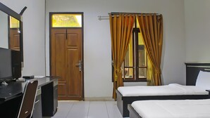 A hotel room with a desk, two beds, a wardrobe, and a window with curtains.
