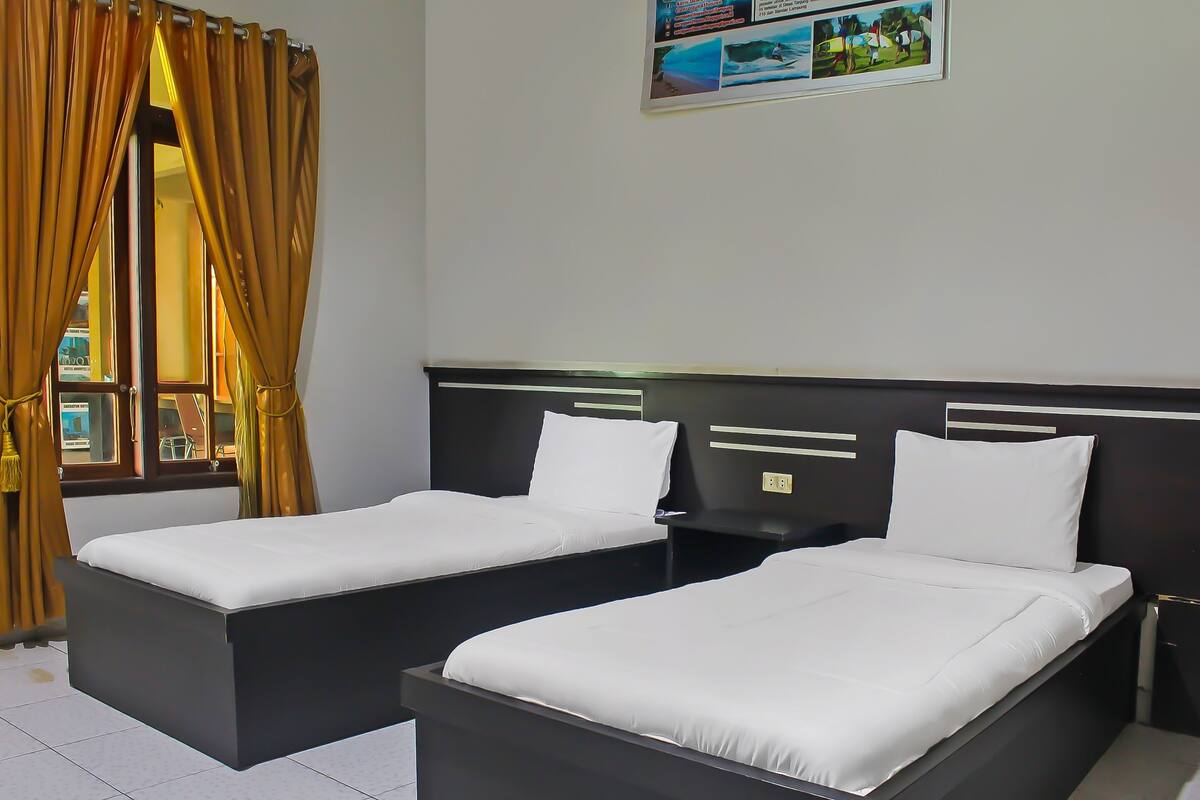 A hotel room with two single beds, a window with curtains, and a wall-mounted artwork.