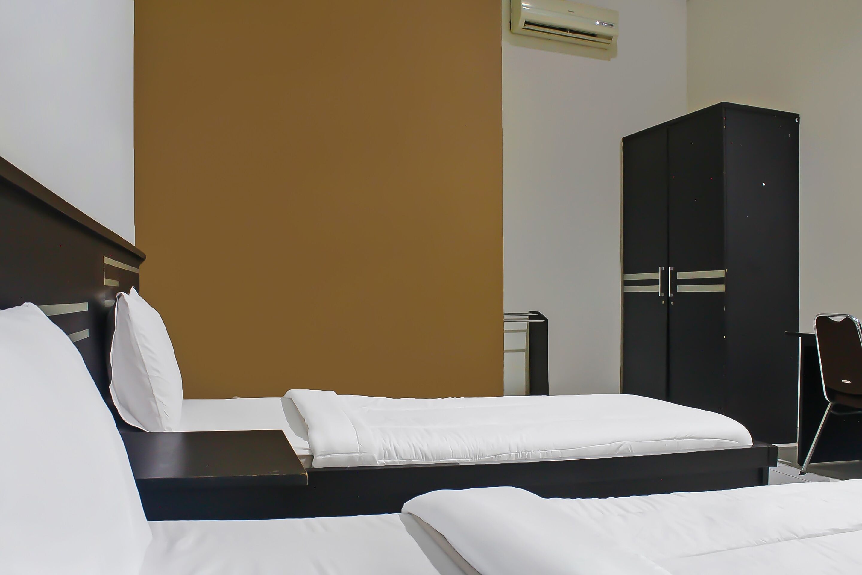 A hotel room with two beds, a wardrobe, and a chair.