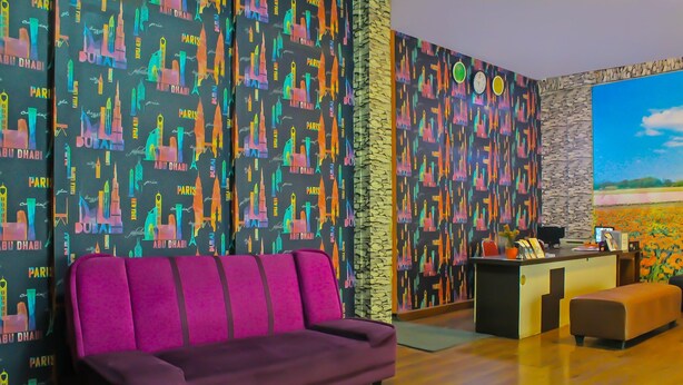A room with a purple sofa, a small desk with a computer, and a large painting of a field.