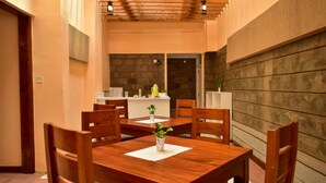 Un coin repas avec une table et des chaises en bois, une petite plante posée sur la table, et une cuisine en arrière-plan.