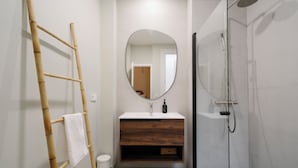 Een badkamer met een houten ladder, een ronde spiegel, een wastafel met houten onderkast, en een glazen douchecabine.