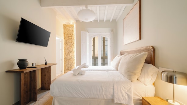 Een hotelkamer met een bed, nachtkastje, lamp en een aan de muur bevestigde televisie.