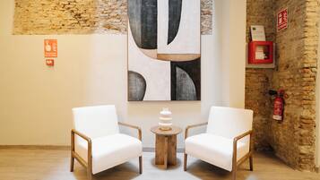 Una habitación con dos sillas blancas, una mesa de madera, un cuadro abstracto grande, un extintor y un cartel en la pared.