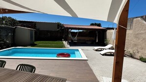 En trädgård med en pool, solstolar, ett träbord och en hängmatta.