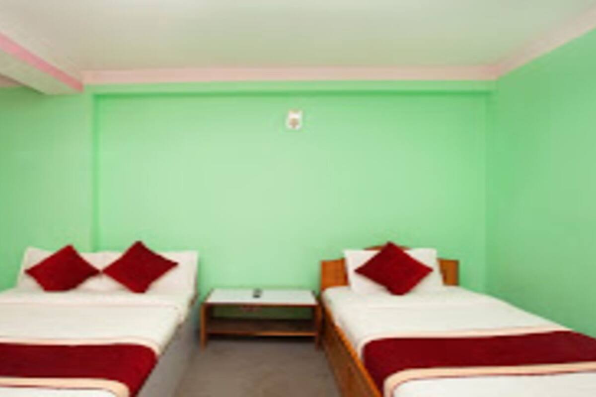Quarto com duas camas, cada uma com roupa de cama e almofadas vermelhas, e uma pequena mesa de cabeceira no meio.