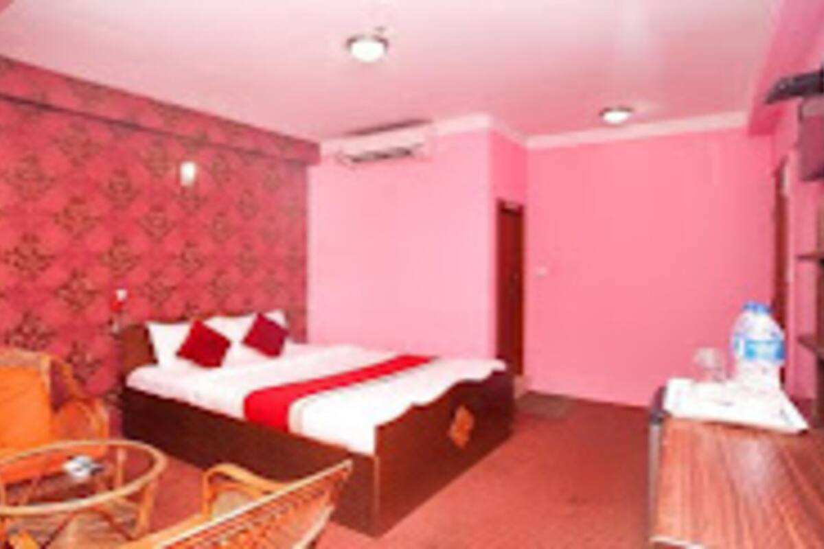 Quarto de hotel com cama, uma cadeira, uma mesinha e uma garrafa de água.