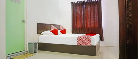 A hotel room with a bed, a trash bin, a green door, and an air conditioning unit.