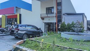 A modern building with a balcony, a parked car, and a fountain in the foreground.