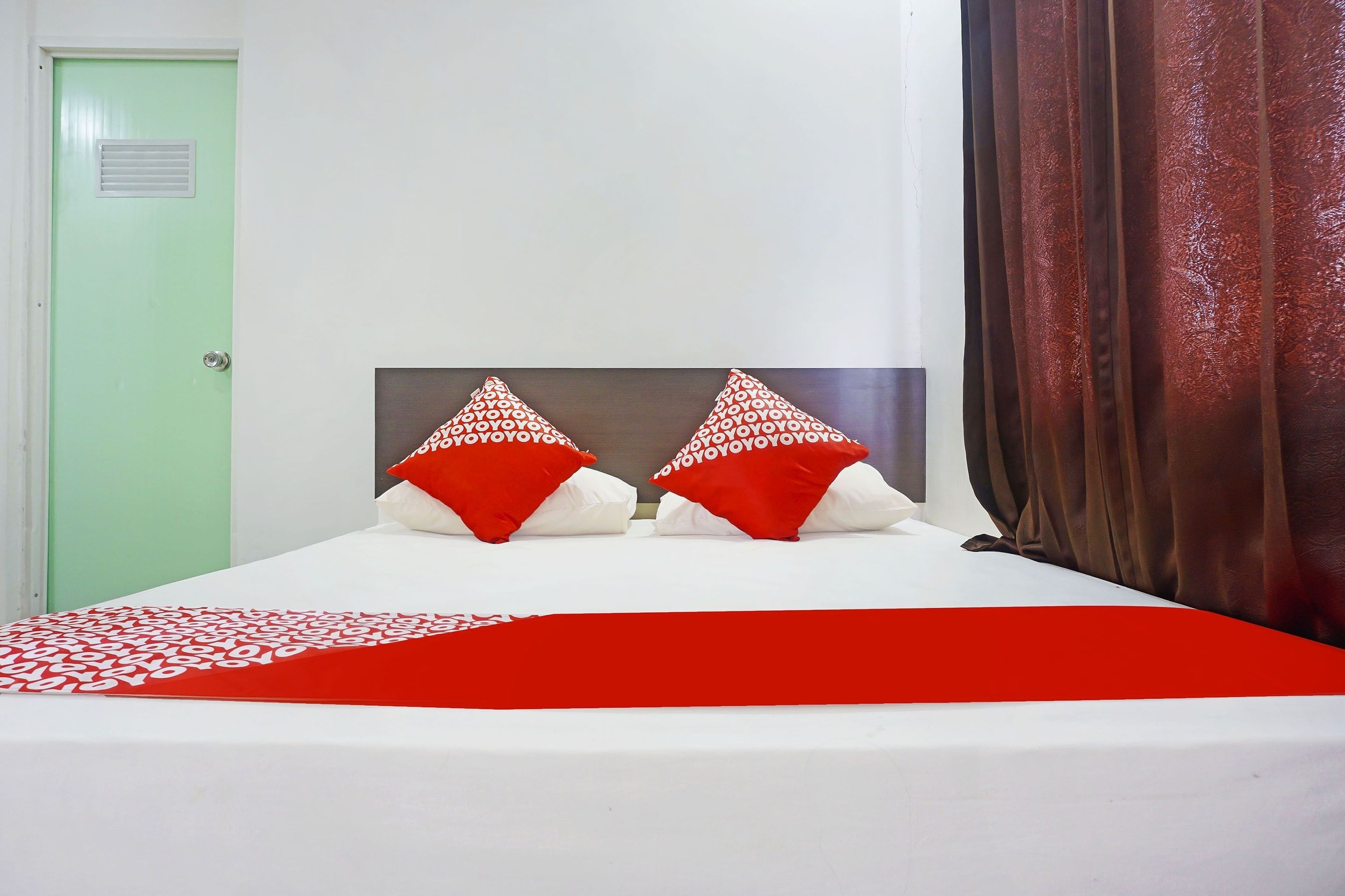 Una cama con una colcha blanca y roja, dos almohadas rojas con texto blanco y una puerta verde.