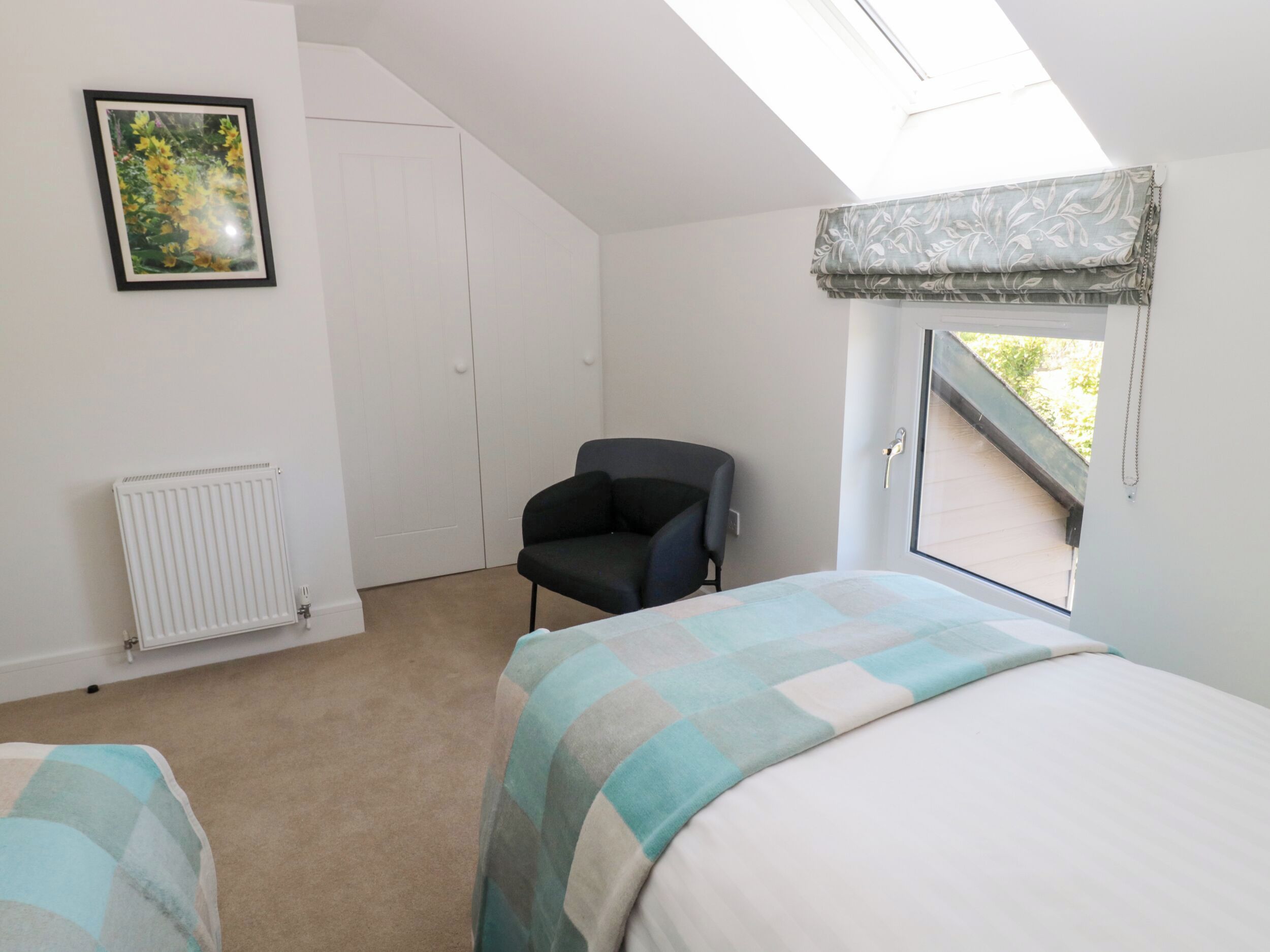 Ein Schlafzimmer mit Bett, Sessel, Heizkörper, Kleiderschrank und einem Fenster mit Blick.
