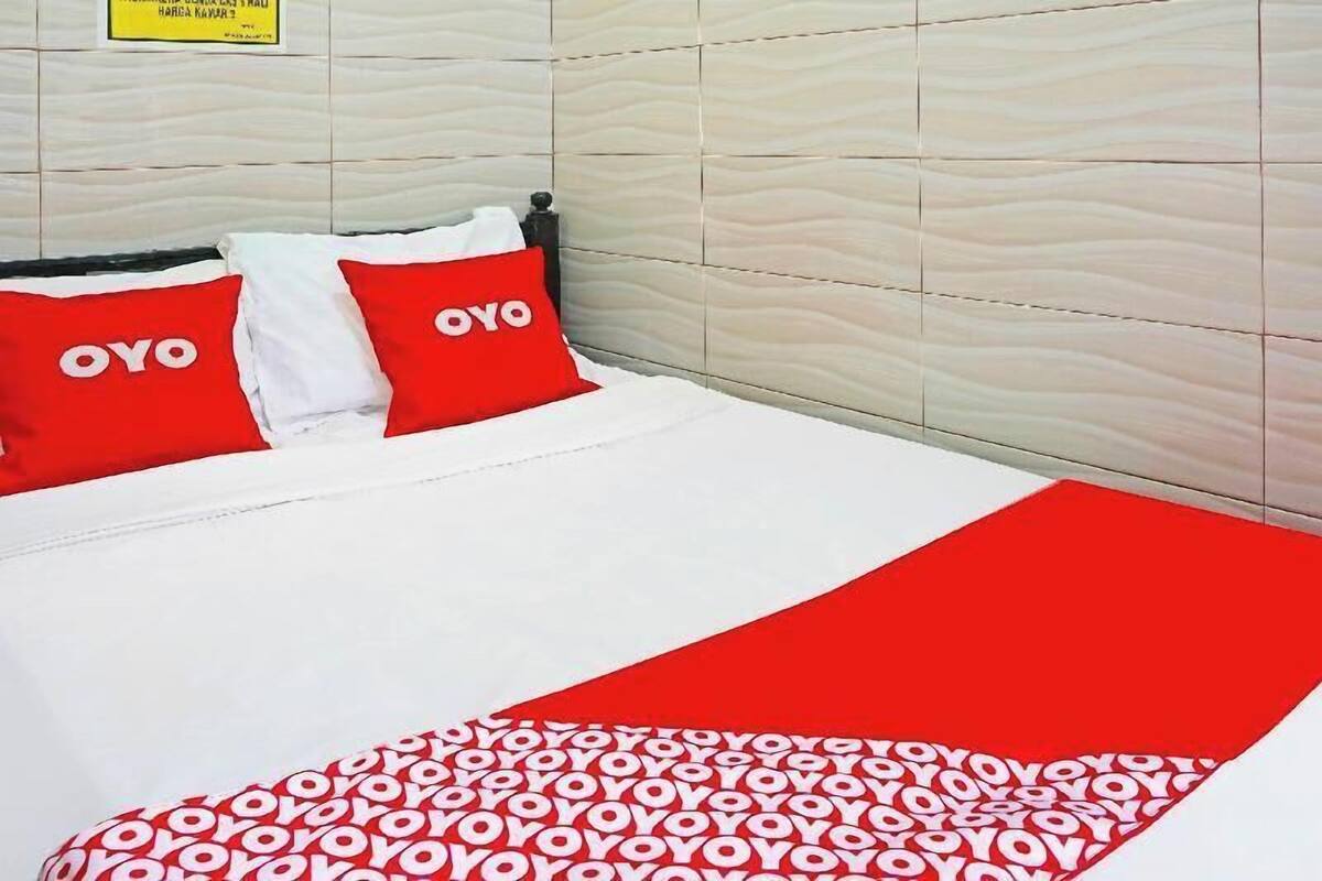 Een hotelkamer met een bed, twee rode kussens met de tekst 'OYO', een wit dekbed en een rode plaid met 'OYO' tekst.