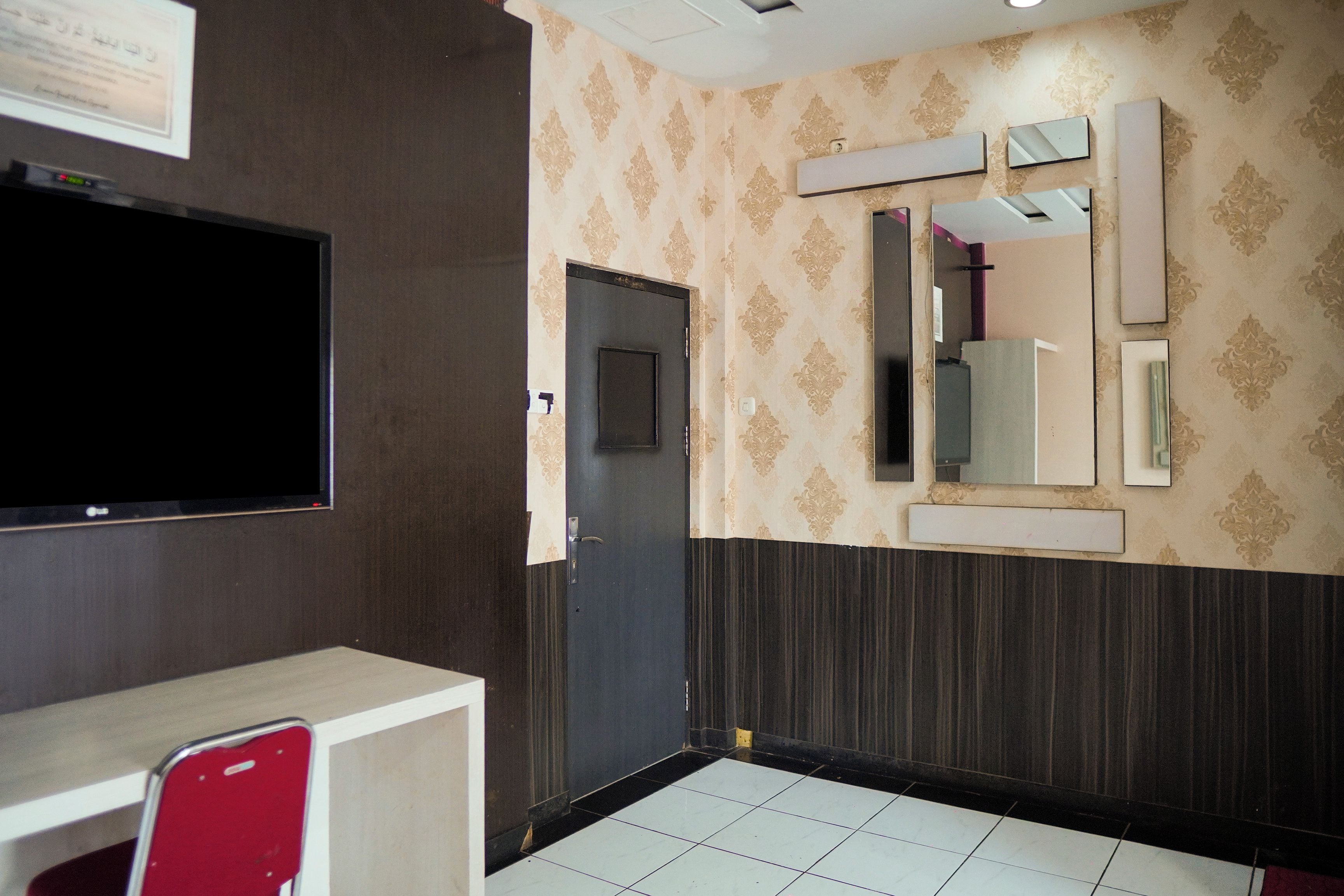 Habitación de hotel con un televisor de pantalla plana montado en la pared, una puerta con un espejo encima y piso de baldosas.