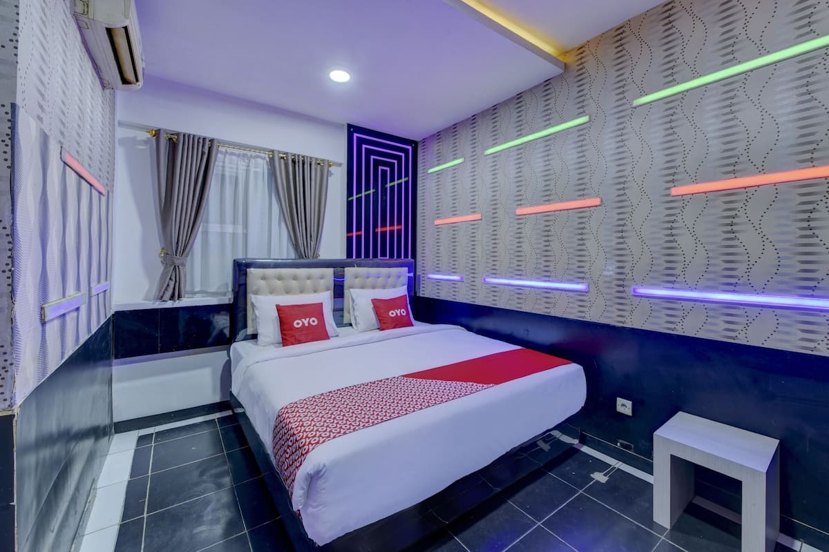 A modern hotel room with a large bed, a small bedside table, and a wall with patterned wallpaper and neon lights.