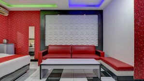 A modern hotel room with a red sofa, a white bed, and a white wall with circular patterns. - Super OYO 4010 Zaara Guest House Syariah (Padang)