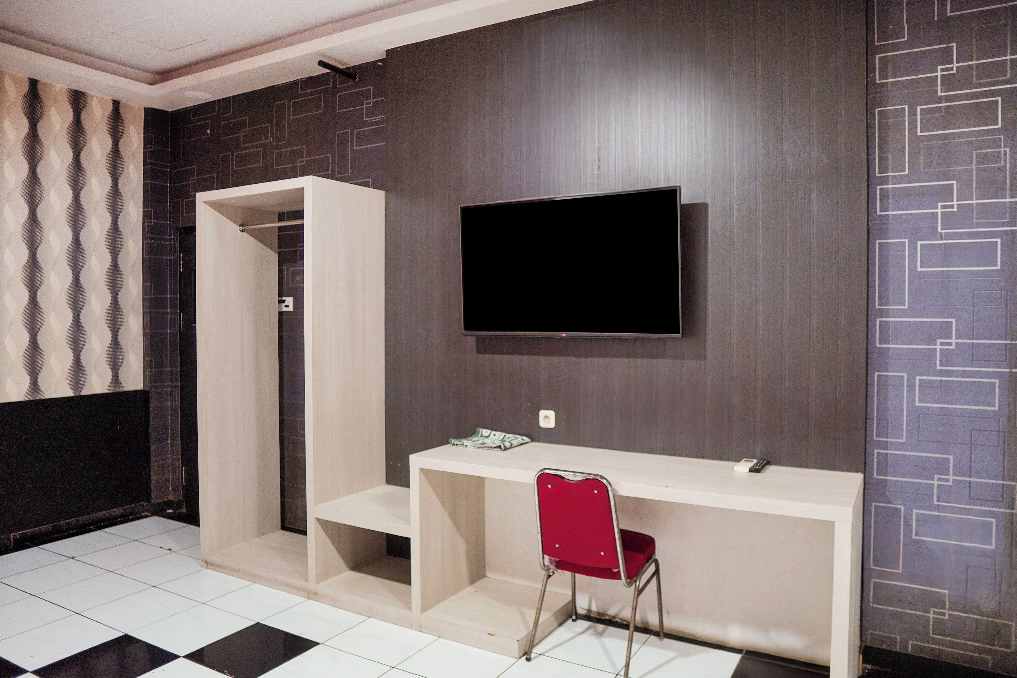 Un baño moderno con piso de baldosas blanco y negro, un tocador blanco con una silla roja y un televisor de pantalla plana montado en la pared.