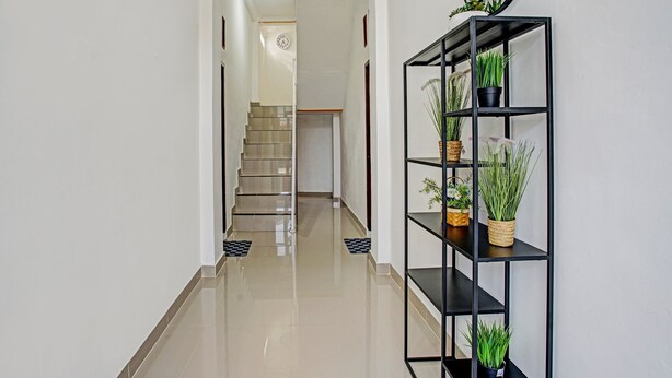 Ein Flur mit poliertem Boden, einem schwarzen Metallregal mit Blumentöpfen und einer Treppe im Hintergrund.