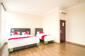 Een hotelkamer met twee bedden, een houten vloer en een airconditioning aan de muur.