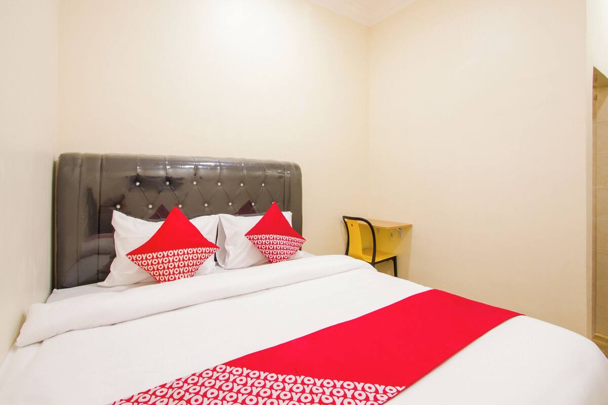 Une chambre d’hôtel avec un grand lit, une tête de lit capitonnée et un couvre-lit à motifs rouges et blancs.