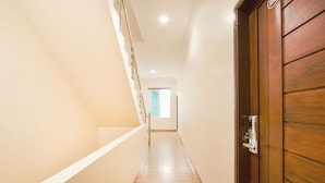 Un couloir étroit et bien éclairé, avec une porte en bois sur la droite et un escalier sur la gauche.