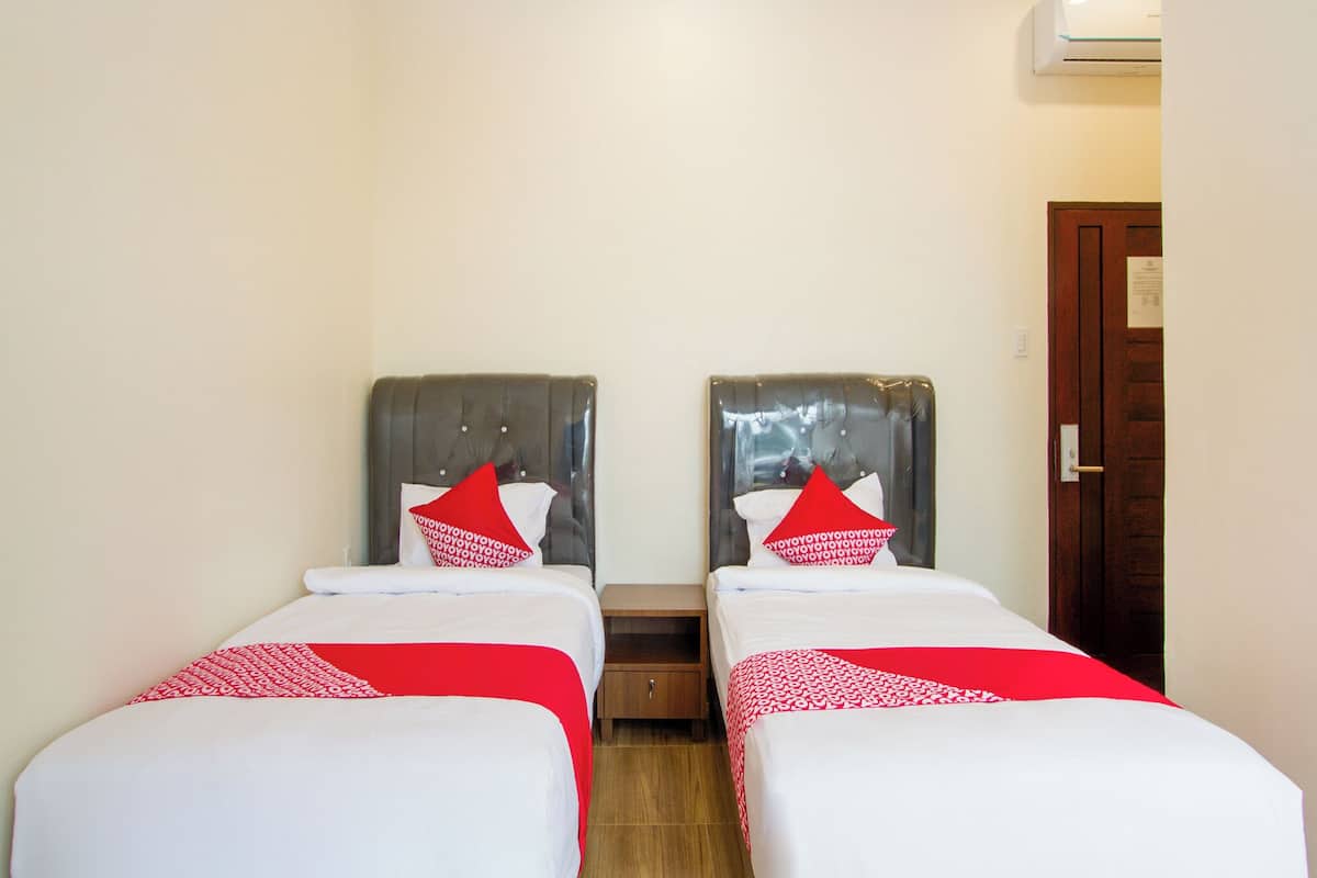 A hotel room with two single beds, each with a red and white pillow, a wooden nightstand, and a door with a sign.