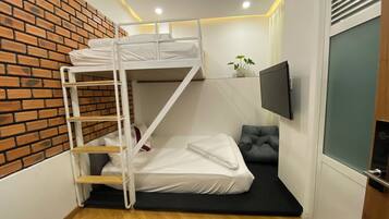 Habitación pequeña con literas, un escritorio, una silla, un televisor montado en la pared y una planta en maceta.