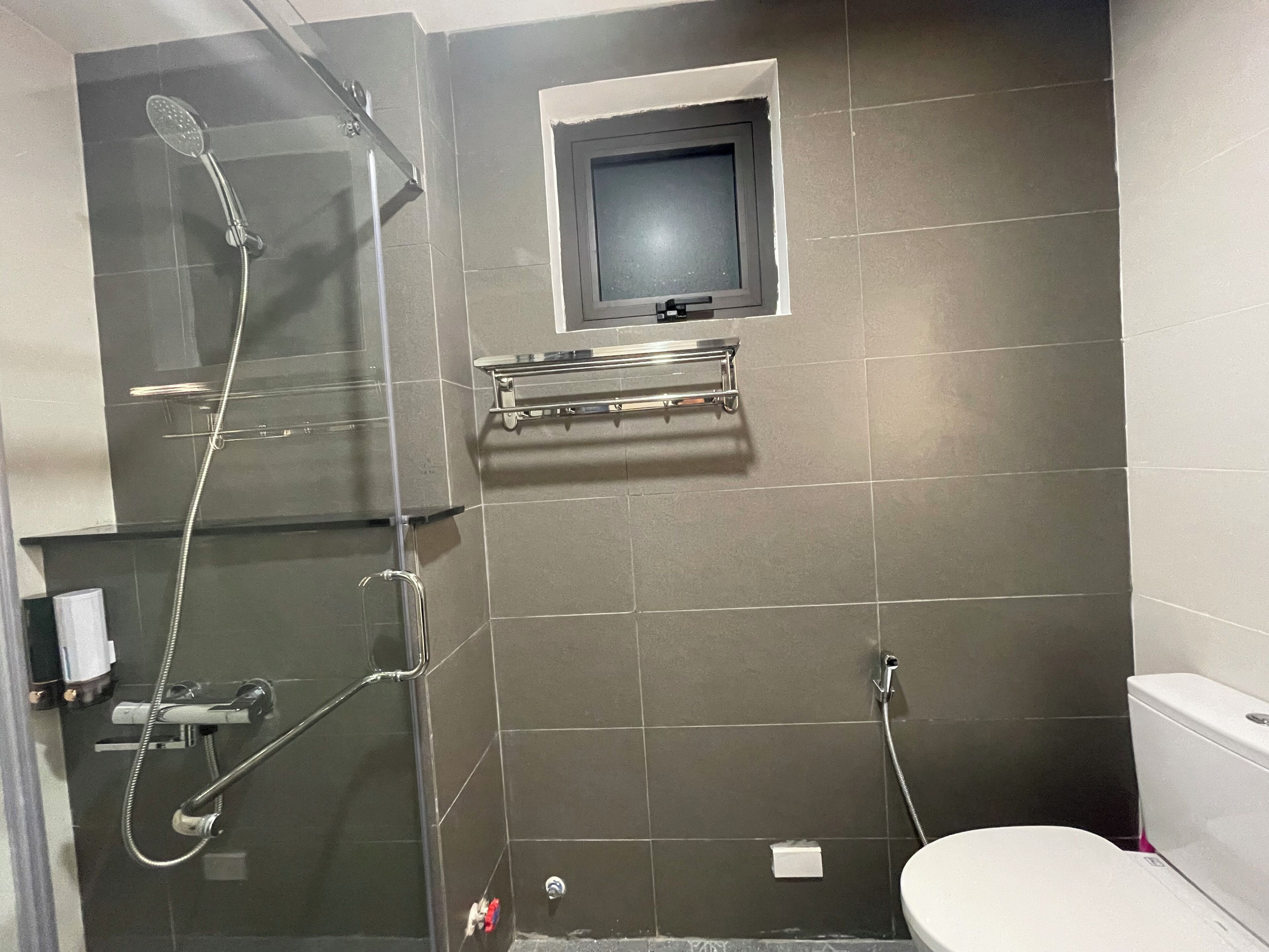 A bathroom with a glass shower enclosure, a toilet, and a small window.