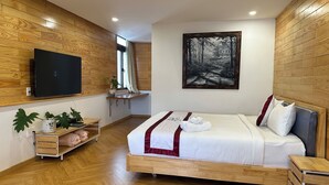 Quarto moderno com piso de madeira, cama com roupa de cama branca e um toque de vermelho, televisão na parede e pintura de uma cena florestal.