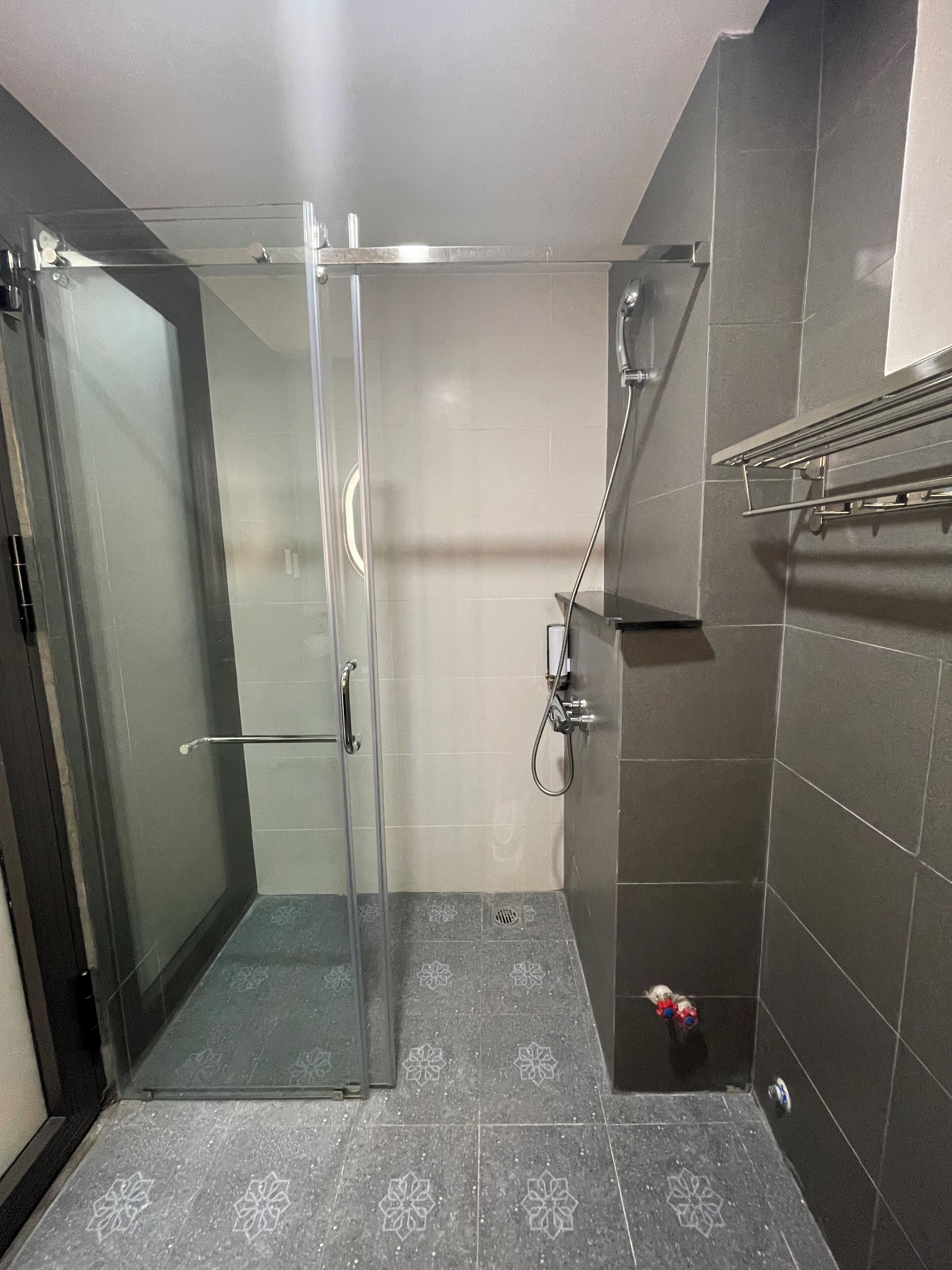 A modern bathroom with a glass shower enclosure, a towel rack, and patterned floor tiles.