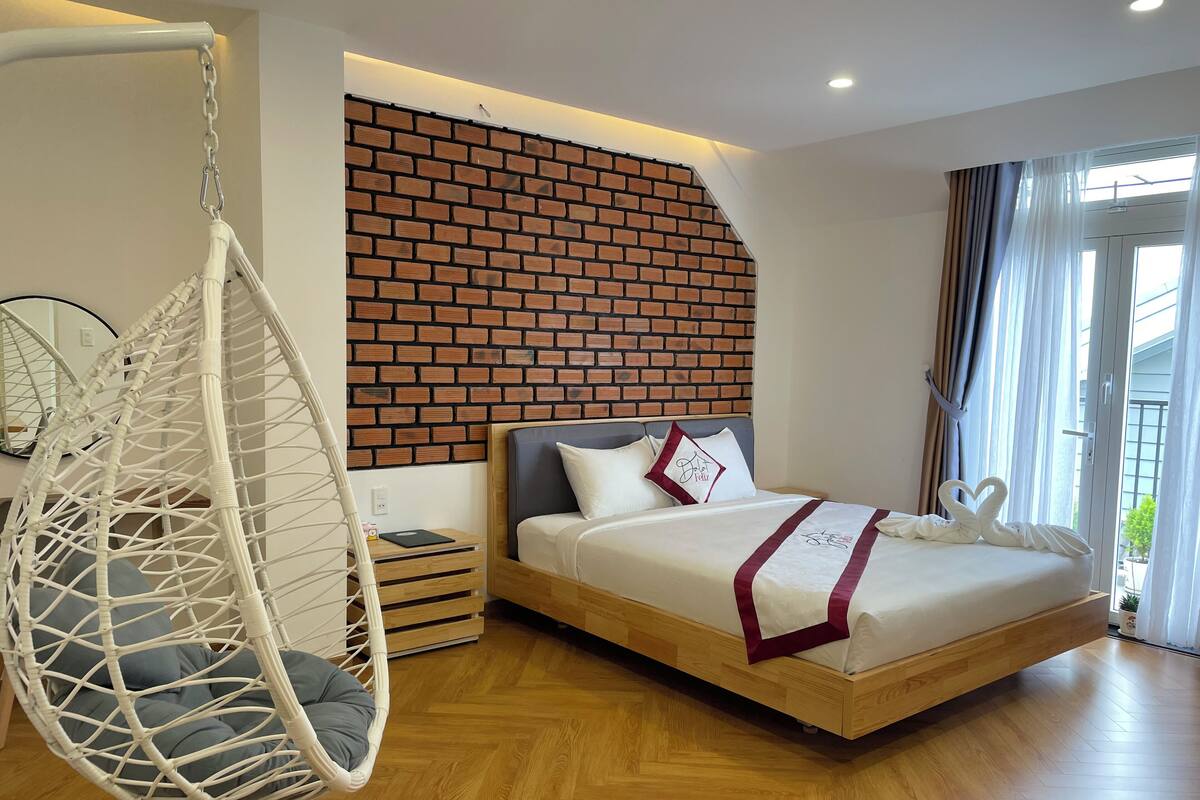 A bedroom with a hanging chair, a bed with a headboard, and a brick-patterned wall.
