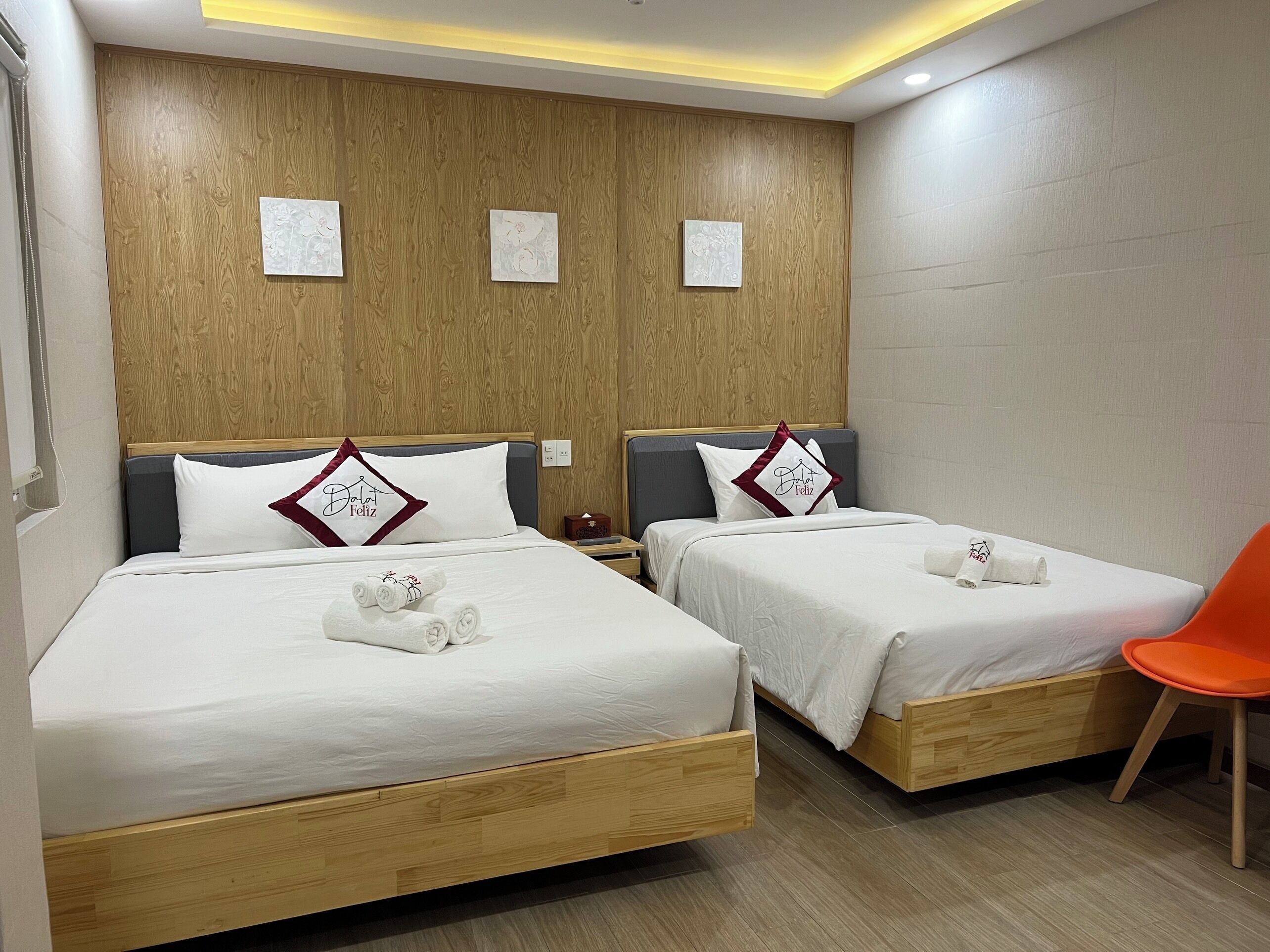 A hotel room with two beds, wooden headboards, and a small orange chair.