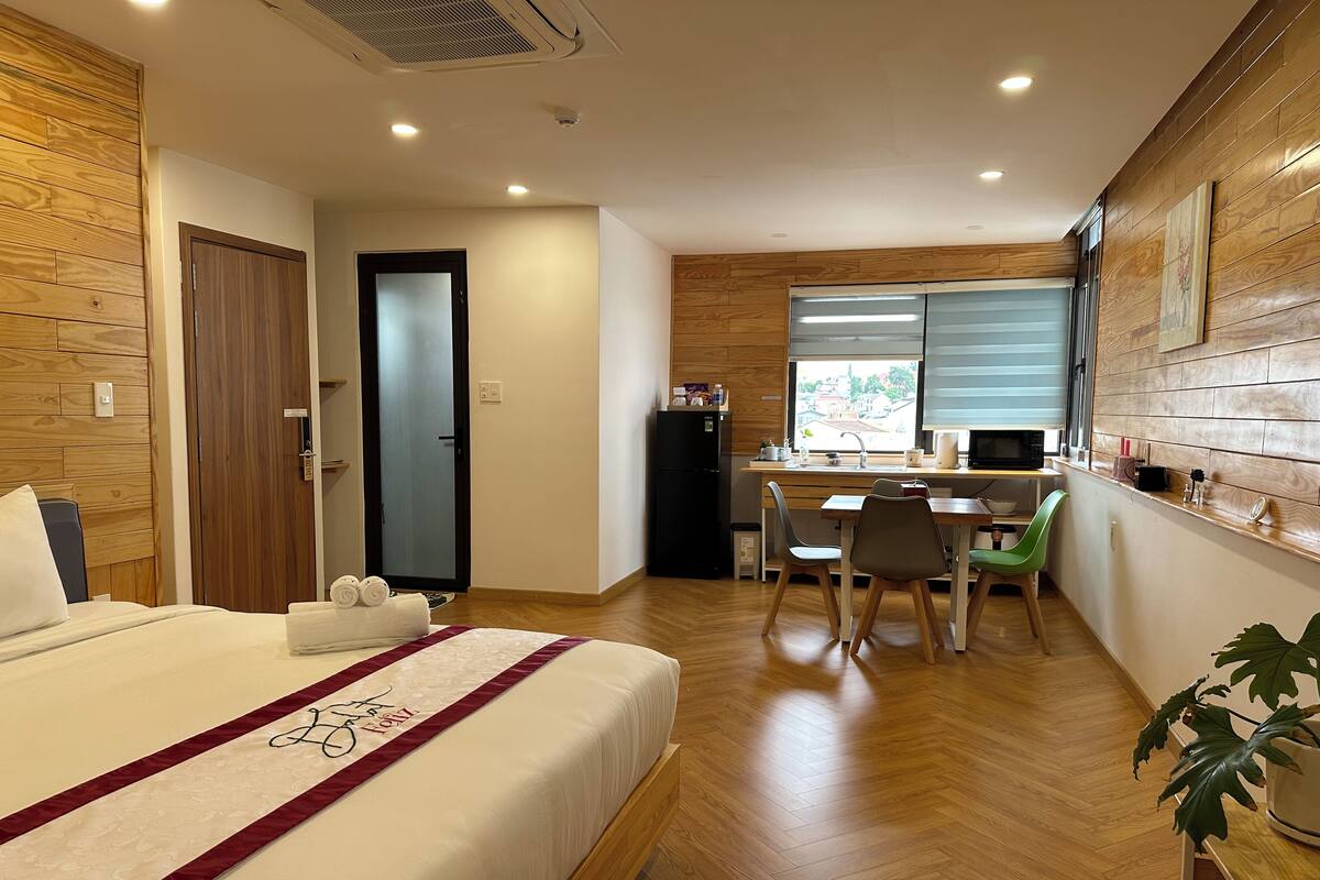A hotel room with a bed, a desk, a chair, a refrigerator, and a window with a view.