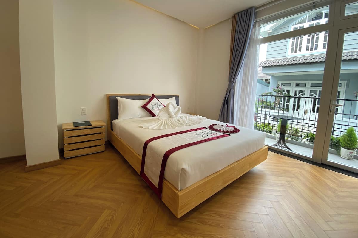 A neatly made bed with a wooden headboard, a bedside table, and a large window with a view of the outside.