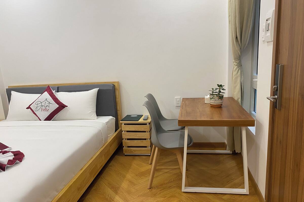 A hotel room with a bed, bedside table, chair, and a small table with a plant.