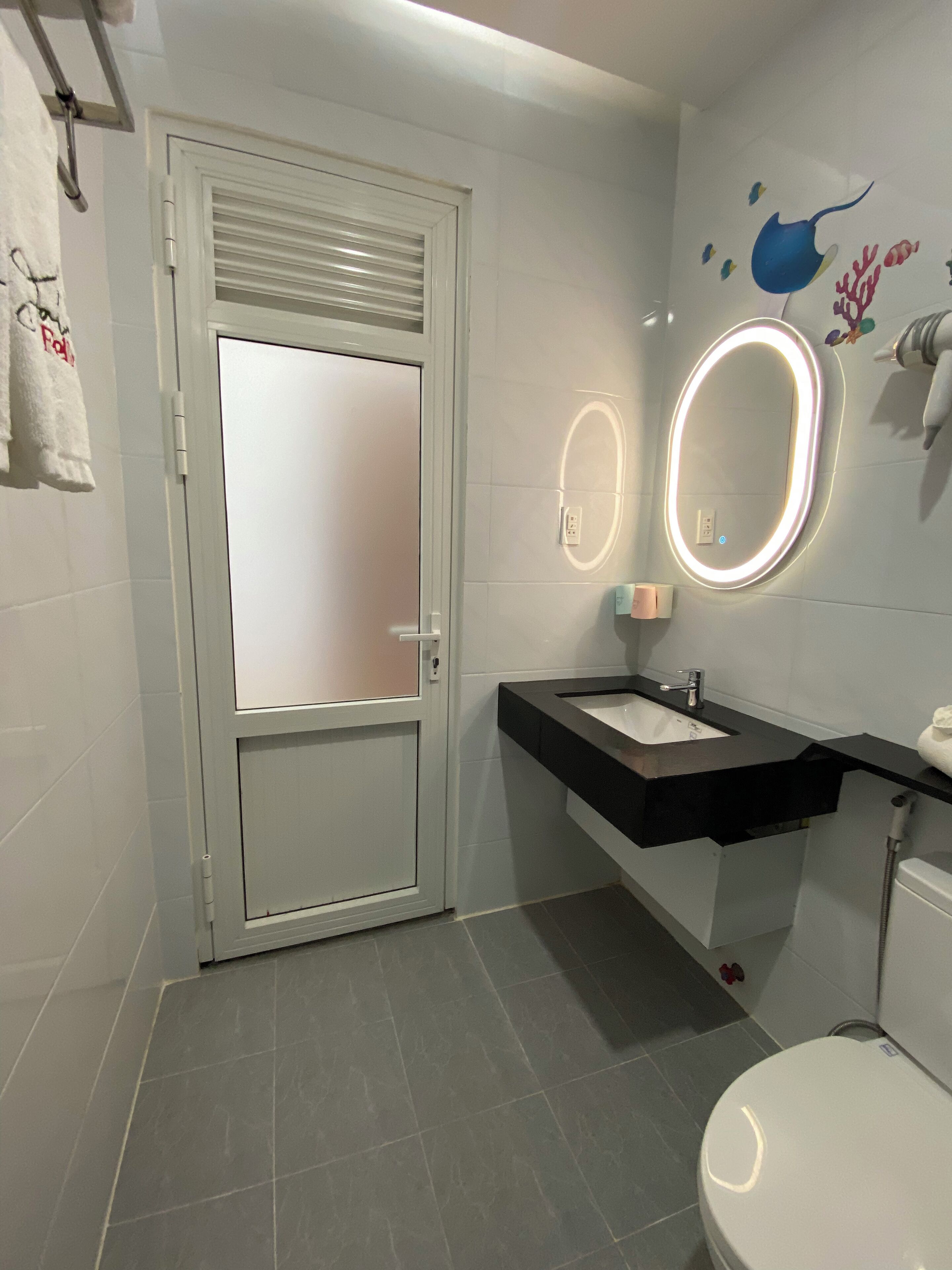 A bathroom with a white door, a black sink, a mirror with lights, and a toilet.