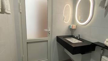 A bathroom with a white door, a black sink, a mirror with lights, and a toilet.