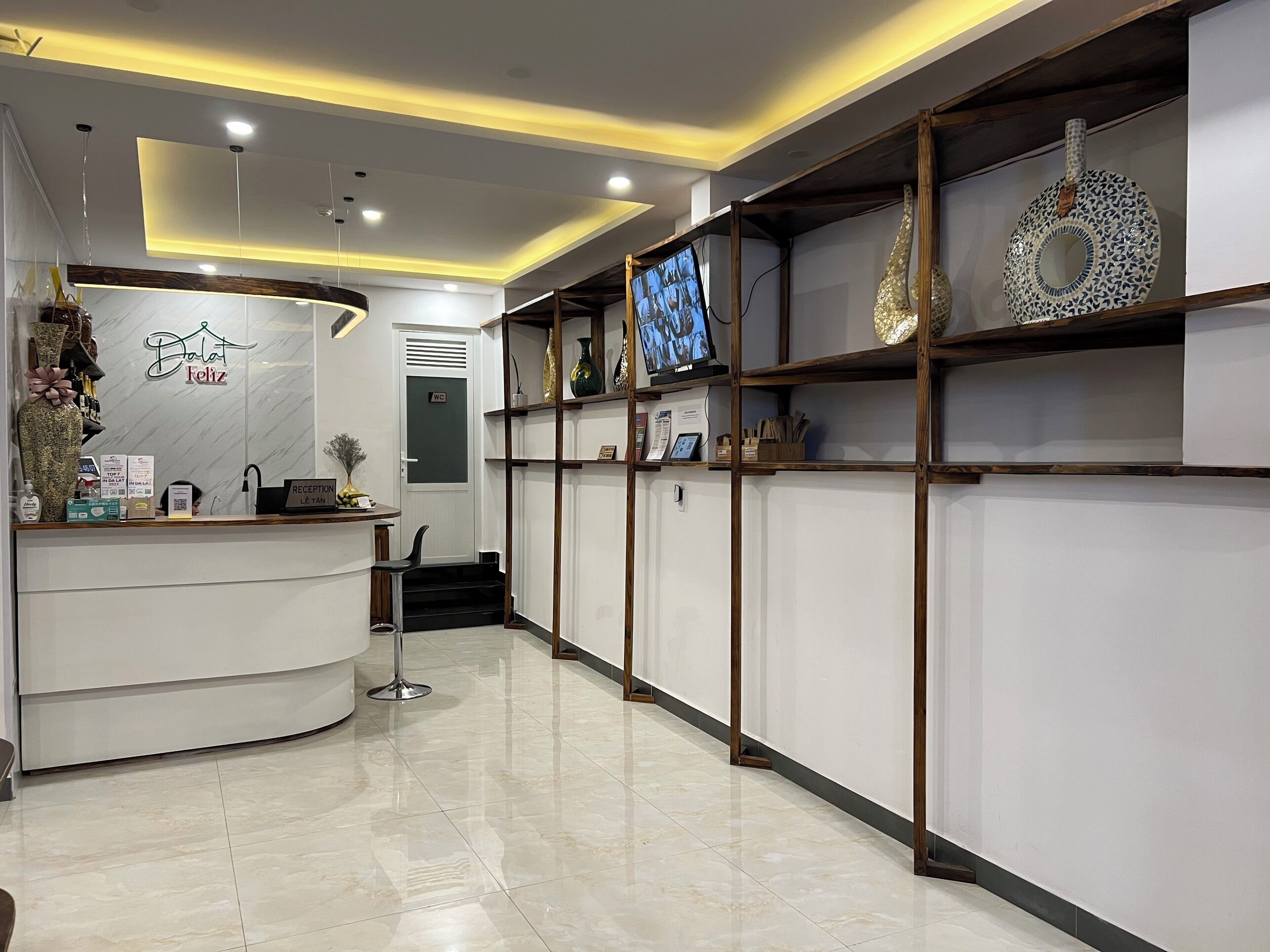 A reception area with a white reception desk, a reception sign, and a TV screen mounted on the wall.