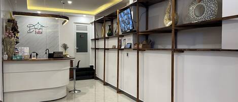 A reception area with a white reception desk, a reception sign, and a TV screen mounted on the wall.
