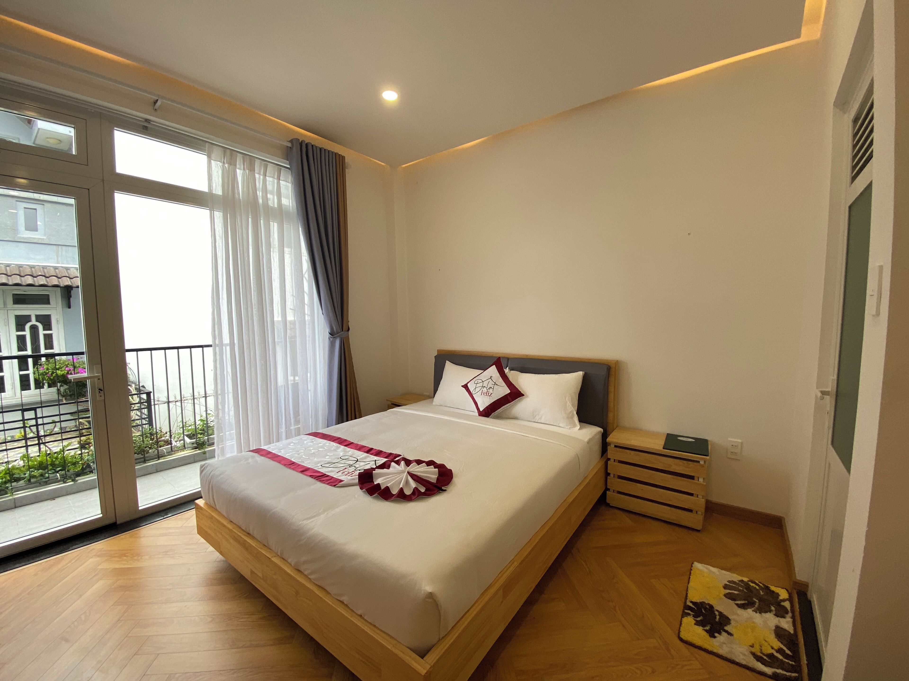 A hotel room with a large bed, a wooden floor, a window with curtains, and a view of the outside.