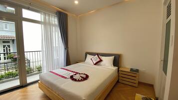 A hotel room with a large bed, a wooden floor, a window with curtains, and a view of the outside.
