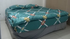 Una cama con colcha color turquesa con personajes de dibujos animados, falda gris y cabecera blanca.
