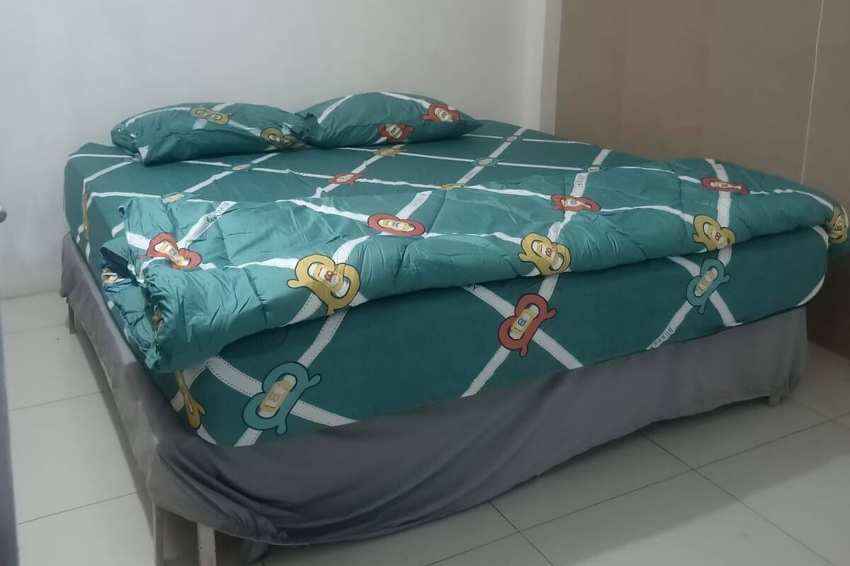 Un lit recouvert d’une couvre-lit turquoise ornée de personnages de dessins animés, avec une jupe de lit grise et une tête de lit blanche.