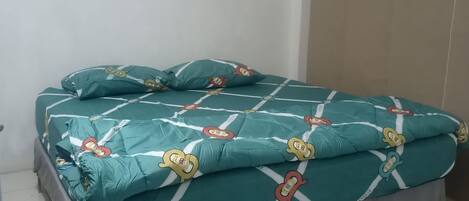 A bed with a teal bedspread featuring cartoon characters, a grey skirt, and a white headboard.